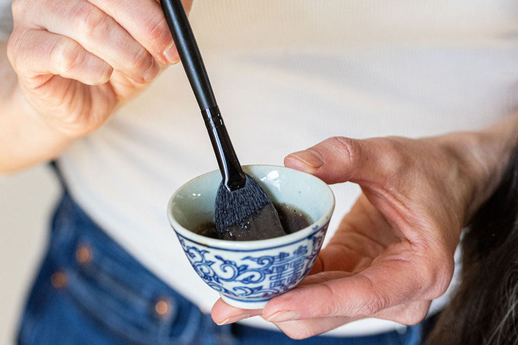Person holding a small blue and white cup with a black spoon, wearing a white shirt and blue jeans.